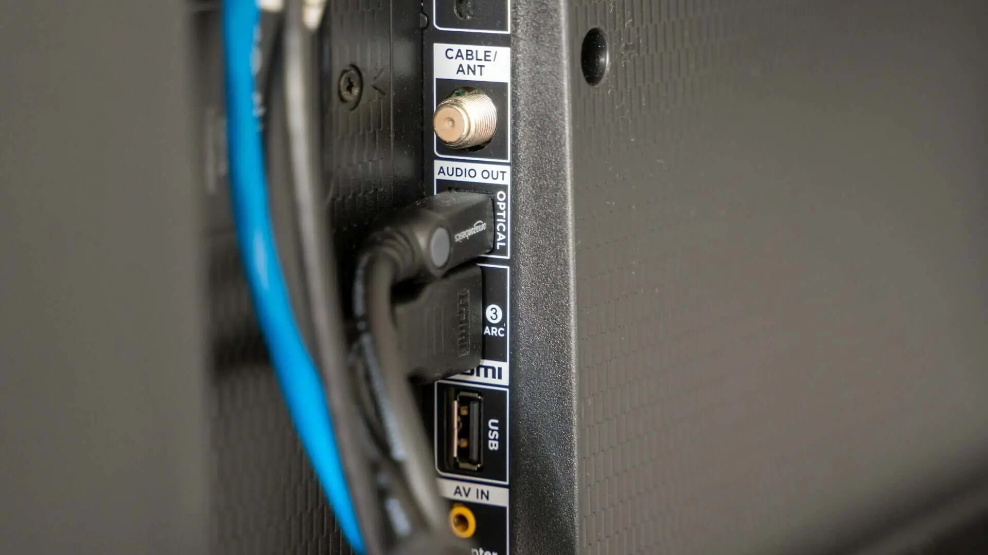 Close-up of various cables connected to the back ports of a flat-screen TV, including HDMI, optical audio, and USB