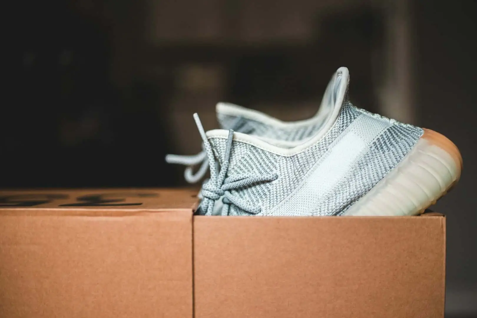 A light grey athletic sneaker sitting on top of a closed cardboard moving box